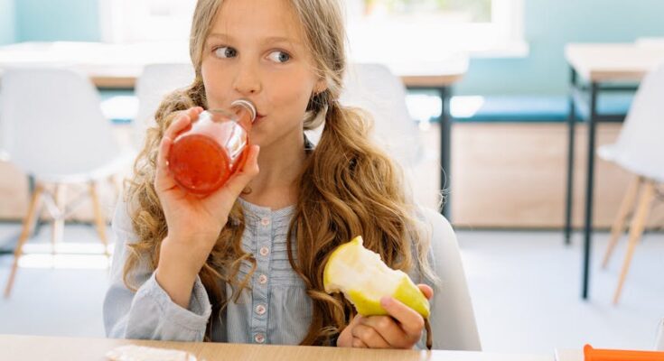 A young girl sitting while drinking a glass of juice