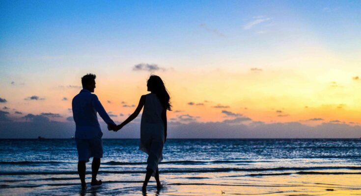 Man and woman holding hands walking on seashore during sunrise