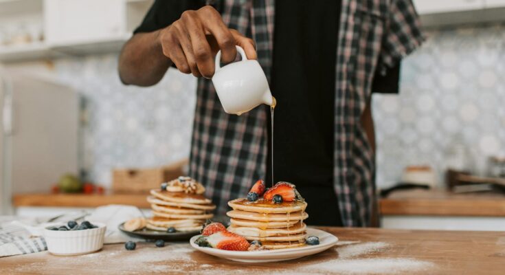 A person pouring maple syrup on a stack of pancakes