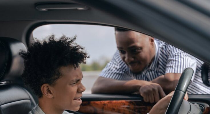 Father looking at a teenager seated on driver s side of a car