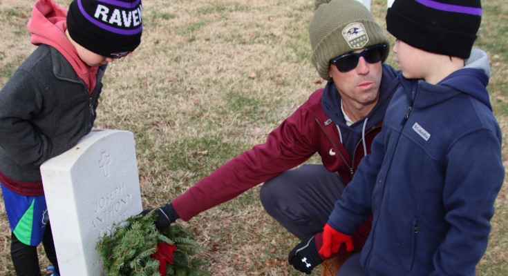 Father places veteran's wreath with sons
