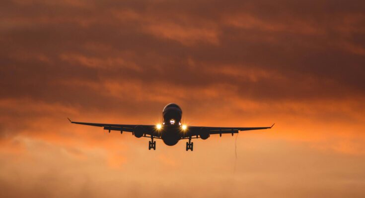 Airplane flying under orange sky at sunset