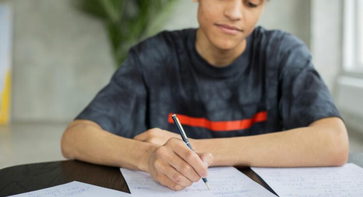 focused black man writing on paper during studies
