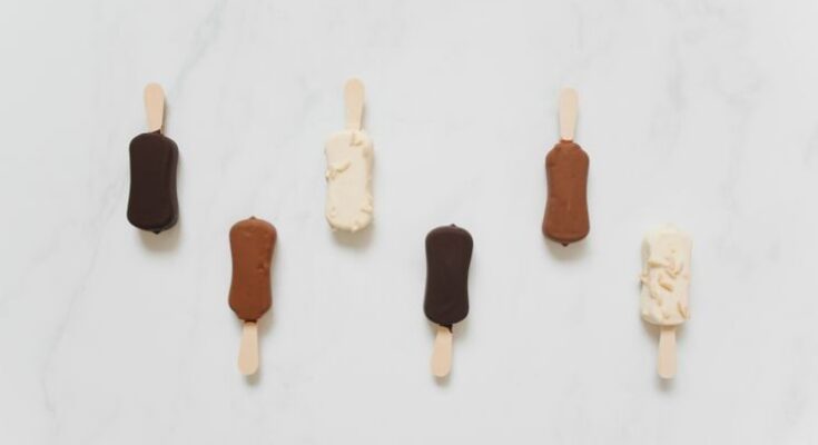 A collection of chocolate and vanilla ice cream bars on sticks on a marble surface.