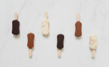 A collection of chocolate and vanilla ice cream bars on sticks on a marble surface.