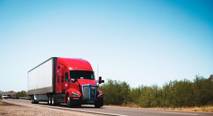 A red semi truck driving down a country road