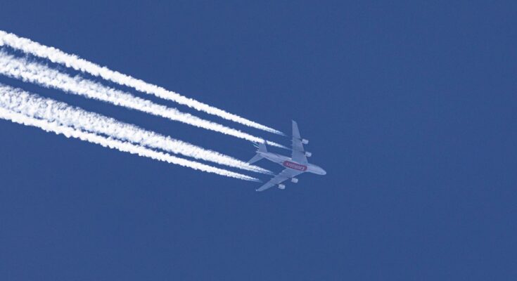 commercial airplane with contrails against blue sky