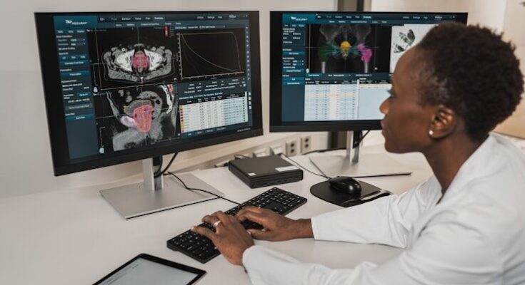 A person in a white coat typing on a keyboard at two medical monitors