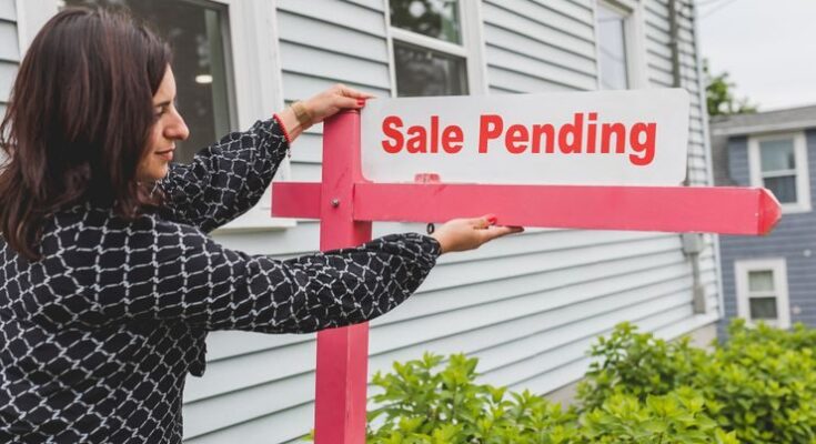 A realtor adjusting a sale pending sign outside a house for sale.