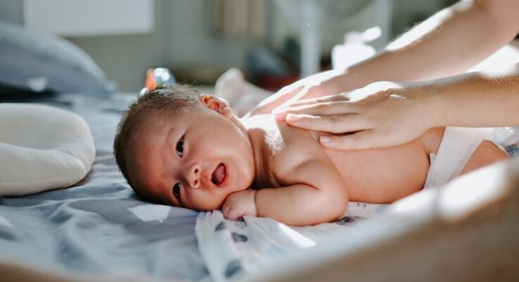 baby laying on bed while woman massaging his back