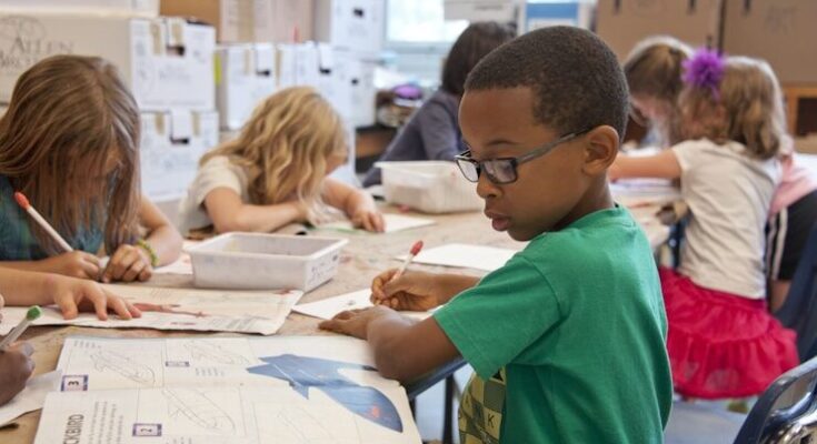 boy in green sweater writing on white paper
