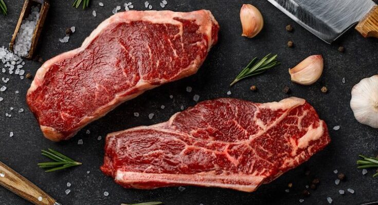 two steaks on a cutting board next to garlic, garlic, and a knife