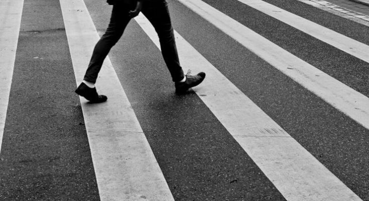 person in black pants and black sneakers walking on pedestrian lane