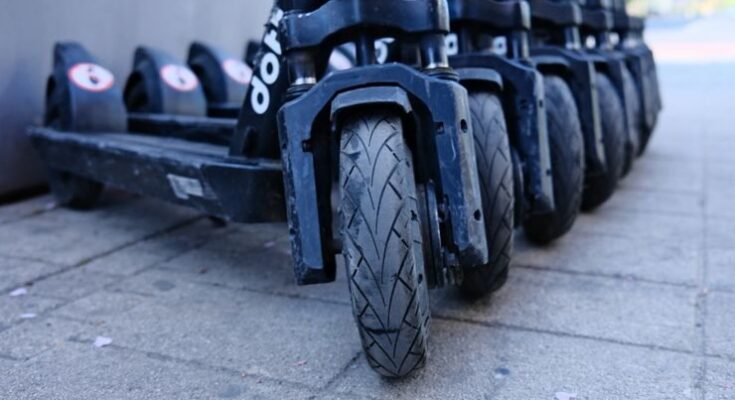 Row of parked electric scooters on a city sidewalk, focusing on wheels.