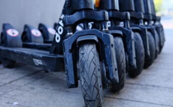 Row of parked electric scooters on a city sidewalk, focusing on wheels.