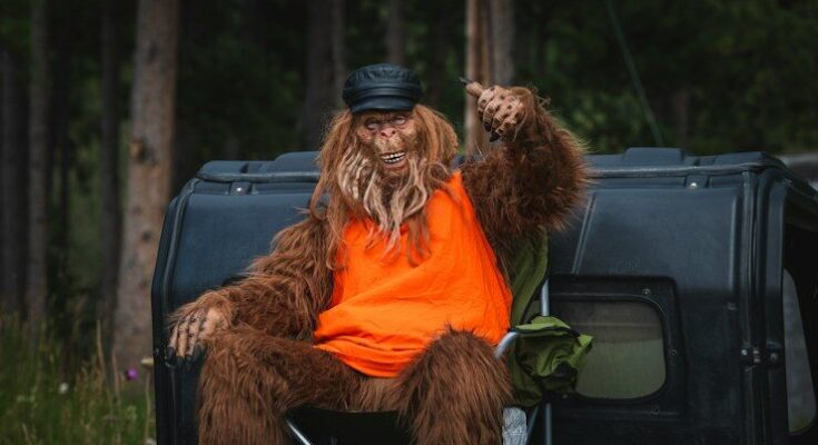 Bigfoot is relaxing by a car in the woods