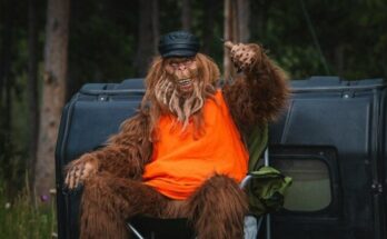 Bigfoot is relaxing by a car in the woods