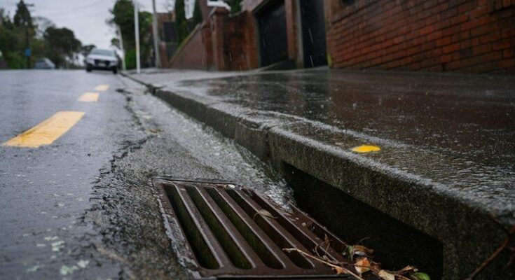 Rainwater flowing into a metal storm drain on a wet city street