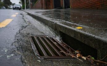Rainwater flowing into a metal storm drain on a wet city street