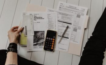 person holding paper near pen and calculator