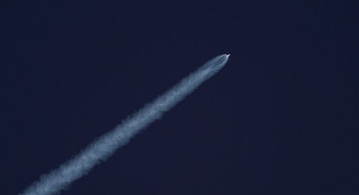A rocket ascends into the sky, leaving a trail of smoke against the clear blue sky.