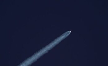 A rocket ascends into the sky, leaving a trail of smoke against the clear blue sky.