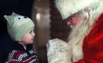 toddler in black sweater standing in front of Santa Claus