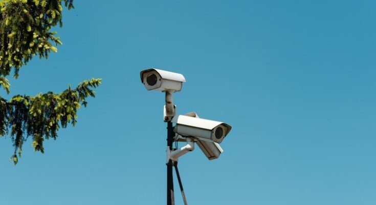 Two white security cameras mounted on a pole against a clear blue sky