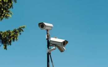 Two white security cameras mounted on a pole against a clear blue sky